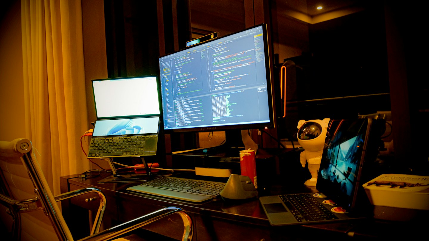 Computer monitors display programming code on a dark wooden desk.